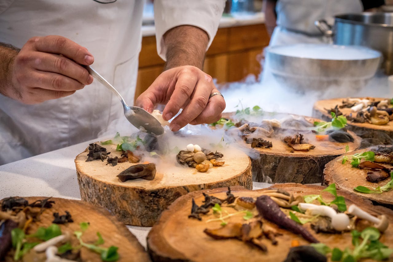 Home A chef artfully plating a gourmet dish with mushrooms and greens on wood slices.